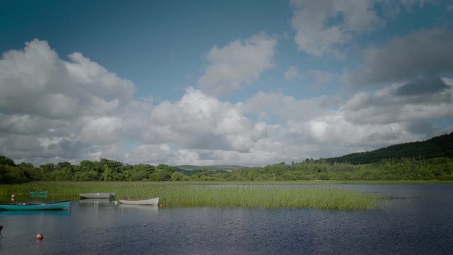 Wooden boats on a still lake in Donegal, Ireland.  Surrounded by green woods and white clouds.