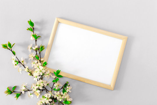 A photo frame and spring floral branches with cherry blossoms. White blank for inspirational or motivational text, quote on gray background. Mockup, flat lay top view, copy space.