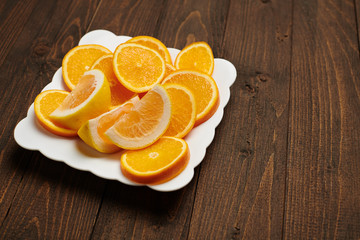 Fresh orange fruits sliced on a plate, dark wooden background - natural and healthy food.