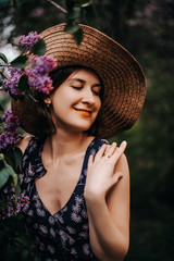 Happy girl in a hat near a lilac