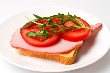 Sandwich of balyk, cheese, bread, tomatoes and arugula on a white plate on a plate view from the side