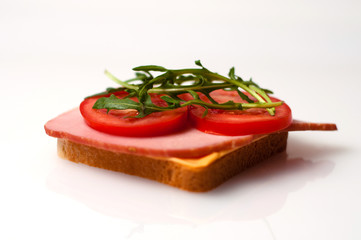 Sandwich made of balyk, cheese, bread, tomatoes and arugula on a white plate side view