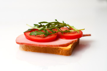 Fototapeta na wymiar Sandwich made of balyk, cheese, bread, tomatoes and arugula on a white plate side view