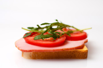 Sandwich made of balyk, cheese, bread, tomatoes and arugula on a white plate side view