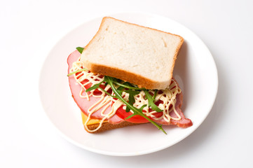 Tasty sandwich with ham or balyk, tomato, arugula, cheese, mayonnaise and white bread for toast on a plate on a white background view from the top flat lay, copy space