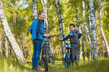 Funny boy cyclist learning to ride a bike with mom in the sunny forest on a bike. Adventure travel.