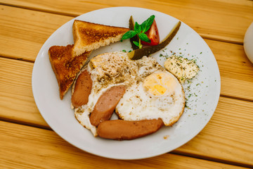 Fried eggs with tomatoes, cucumbers and cheese for breakfast. Scrambled eggs with sausages and tomatoes in a cafe. Comprehensive breakfast with eggs, ham, vegetables and toast.