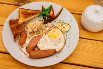 Fried eggs with tomatoes, cucumbers and cheese for breakfast. Scrambled eggs with sausages and tomatoes in a cafe. Comprehensive breakfast with eggs, ham, vegetables and toast.