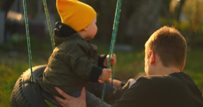 Happy dad rolls a cheerful son on a swing in a park on an oak tree. The concept of a happy family. Single father. Slow motion father and son on a swing on father day.