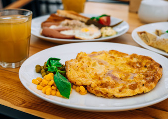 Breakfast in the cafe: omelet with sausages, toast and a glass of fresh juice. Delicious omelette with ham and peas for garnish. Omelet and a glass of juice in a restaurant.
