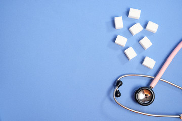 Pink stethoscope, sugar cubes on a blue background, diabetes. Space for text