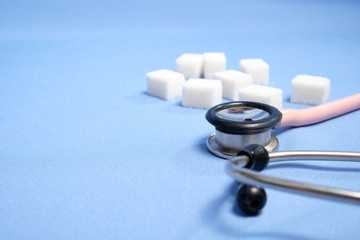 Pink stethoscope, sugar cubes on a blue background, diabetes. Space for text, selective focus