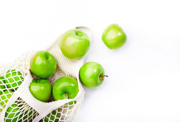 Organic green apples in reusable eco-friendly string mesh bag. Zero waste, plastic free and sustainable lifestyle concept. White kitchen table background, copy space, top view
