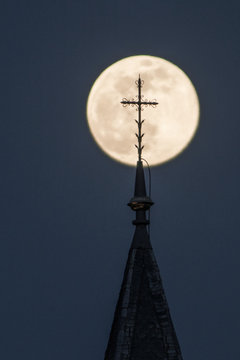 Church tower with cross in front of the super moon