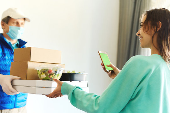 Woman Receiving Packages From Delivery Man. Courier In Uniform Face Mask Gloves Holding Paper Boxes For Take Out Food And Bags. Delivery Food Service At Home, Shopping Order Online From Smartphone