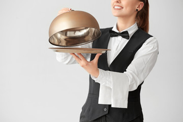 Beautiful female waiter with tray and cloche on grey background