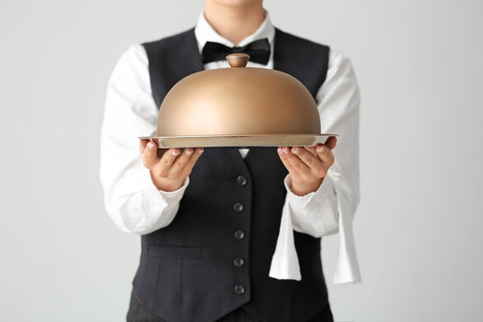 Beautiful female waiter with tray and cloche on grey background