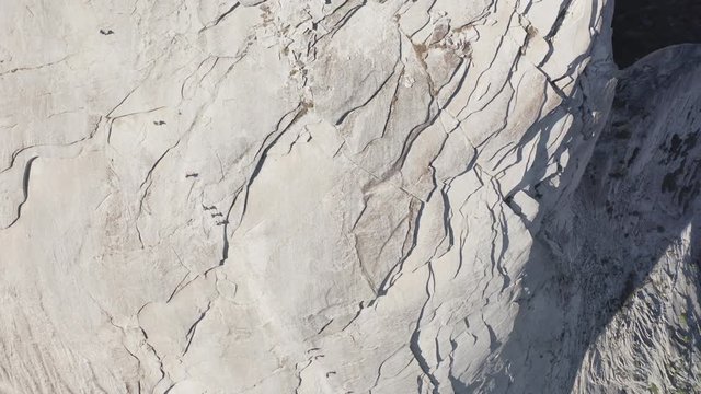 Top aerial footage of a group of tourists climbing a specially equipped trail which goes up a smooth stone slope to the top of the famous Half Dome mountain, located in Yosemite National Park, USA. 4K