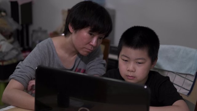 Asian child and mother using laptop for online schooling amid coronavirus pandemic
