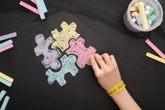 top view of woman in bracelet drawing puzzle with chalks rof World Autism Awareness Day - Powered by Adobe