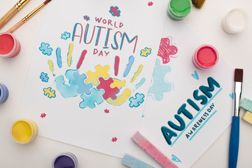 top view of cards for World Autism Day lettering and painting of puzzle and hand prints on white with paint brushes, chalks and paints