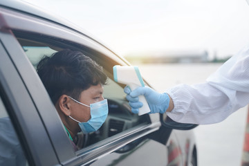 Medical worker in protective suit use infrared forehead thermometer (thermometer gun) to check body...