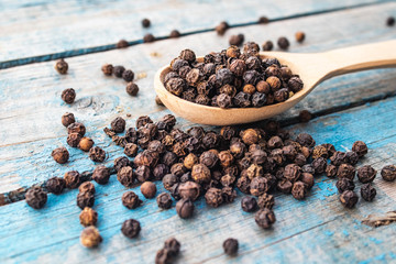 Dry black pepper in a wooden spoon near black pepper scattered on blue boards.