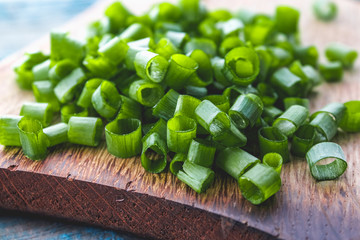 Sliced green onion rings on a cutting board on a background of old blue boards.