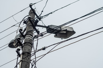 Old concrete lamppost with chaotically hung wires.