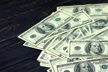 Pile of one hundred dollar bills on black wooden background. 