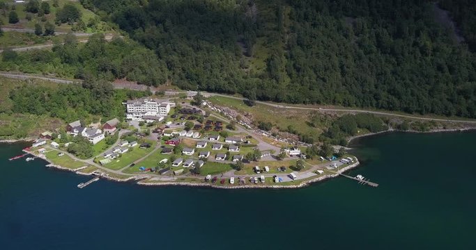 Aerial view of the Geirangerfjorden Feriesenter - a campise on the shore of the Geiranger fjord. Rows of cabins, camping cars, caravans, and tents arranged orderly on the shoreline.