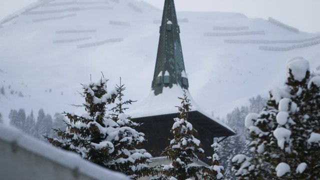 Pan from a curch surrounded by trees to a mountain, covered with snow