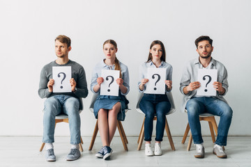 Group of employees holding cards with question marks while waiting for job interview