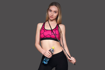 Sportswoman with a skipping rope on a gray background with a bottle in her hands