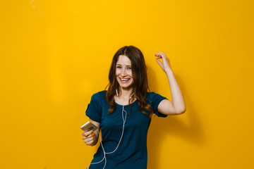 Portrait of a beautiful girl holding a cell phone,  and listen to music in the headphones over a...