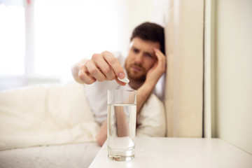 Fototapeta na wymiar Hangover. Man Puts Pill in Water. Man in Bed Morning Headache. Man Using Aspirin. Glass of Water Close Up.