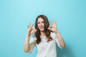Fototapeta premium Portrait of a beautiful young girl showing gestures and is happy over blue background