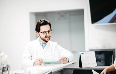 Naklejka na ściany i meble male doctor in a white coat is studying documents medical history, a work schedule in a medical office.