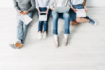 Cropped view of employees with resume and digital devices sitting on floor in office