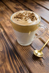 Dalgona coffee in the glass cup in the brown wooden  background. Location vertical.