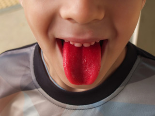 the boy stickig out his bright red tongue after sweets and ice cream