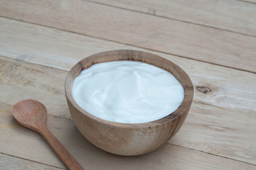 Natural homemade plain organic yogurt in wooden bowl and wood spoon on wood texture background