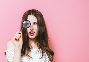 Image of a brunette woman holding a magnifying glass on a pink background