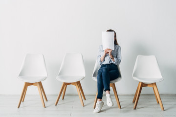 Young woman covering face with resume while waiting for job interview in office