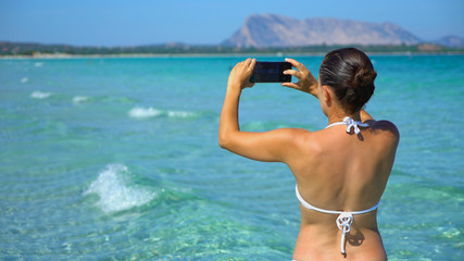 Young woman uses a smartphone to capture a beautiful view at the beach