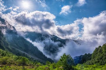 Heavy fog, clouds and bright blue sky with the sun in mountains in the summer or spring. A layer of melting snow in the summer in high mountains.