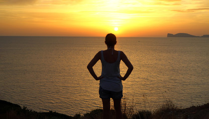 Fototapeta premium Silhouette of female tourist enjoying beautiful view under the sunset, Sardinia, Italy,