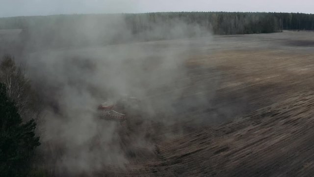 Aerial view of a moving tractor with a plow raising dust preparing the field for sowing