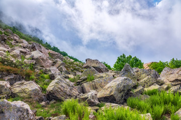 Majestic view of high mountains hidden by clouds and fog from a cliff with large stones.