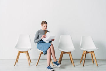 Beautiful candidate holding resume while sitting on chair in office